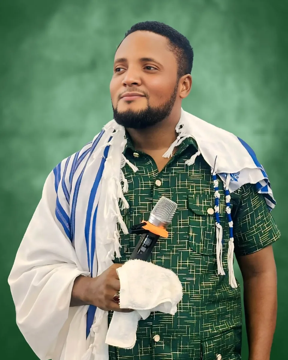 Apostle A.A. Austin, wearing a prayer shawl and holding a microphone
