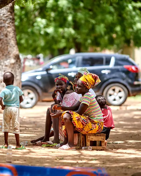 Women and children sitting together and talking under a tree