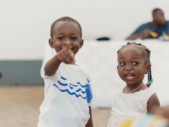Two young children smiling, one pointing at the camera