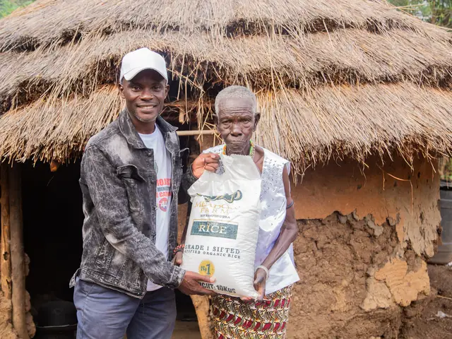 A man handing a bag of rice to an elderly woman outside her thatched home